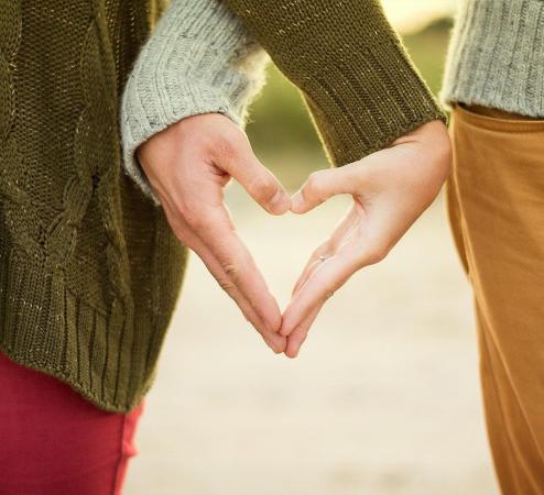 Two people forming a single heart shape with one hand each