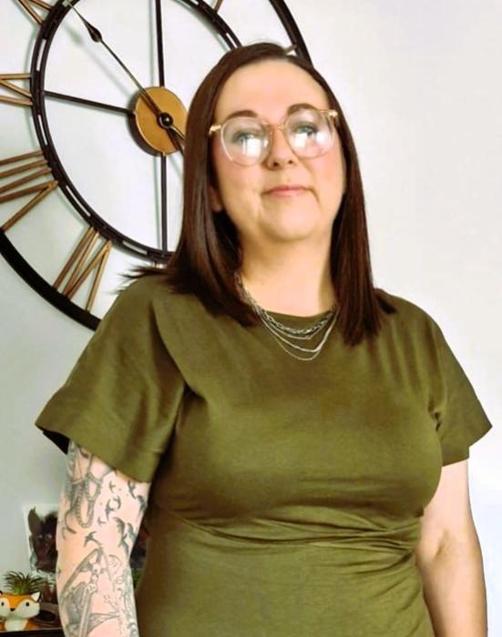 Photo shows new Manager a lady in olive green dress standing in front of a clock