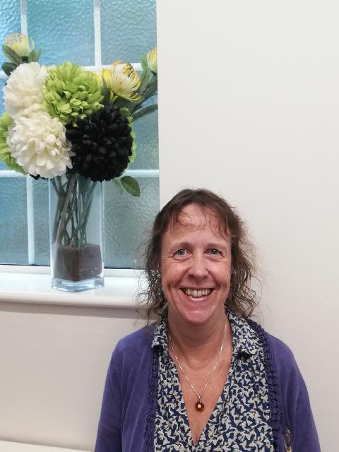 Photo shows lady smiling wearing flower print blouse and cardigan 