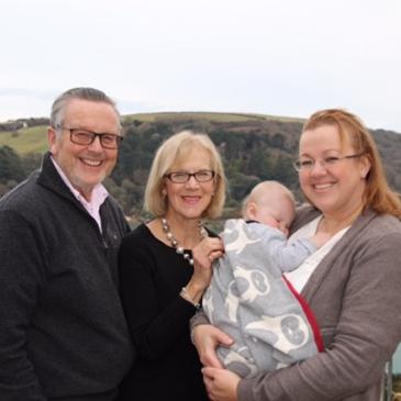 Managing Director Louise holding her son as a baby with her parents. In the background Salcombe