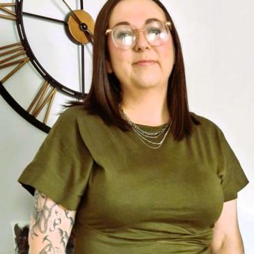 Photo shows new Manager a lady in olive green dress standing in front of a clock
